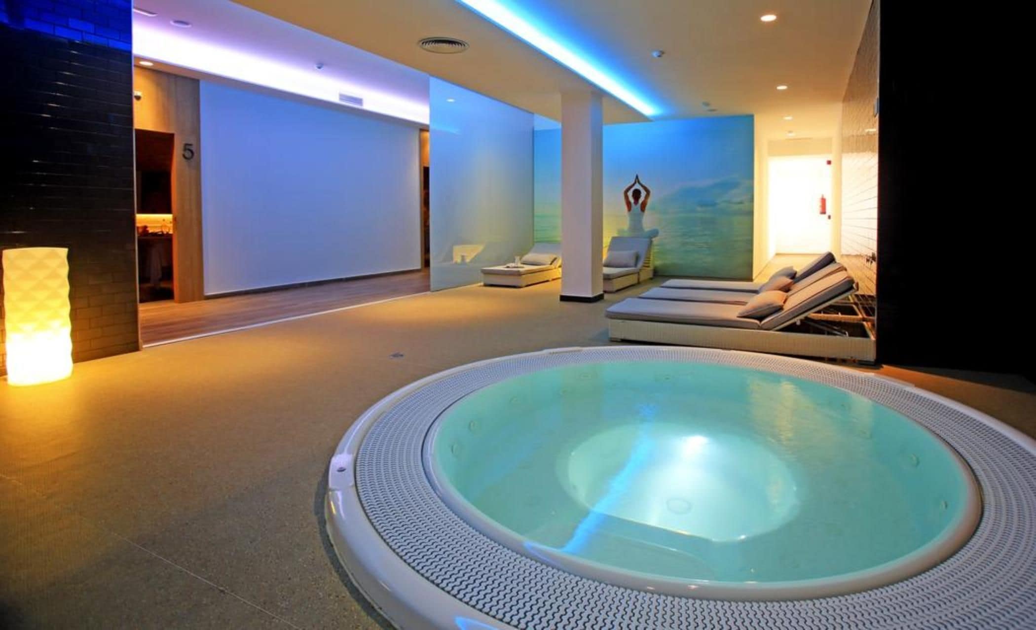 Un área de piscina interior moderna con un jacuzzi, sillas de descanso y un jardín interior tranquilo.