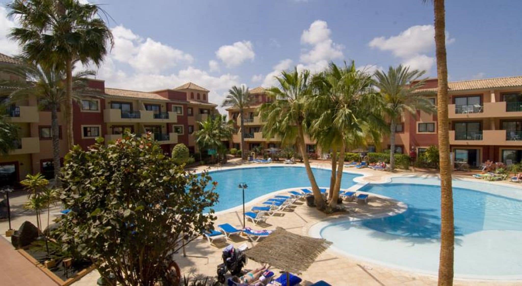 Ein Resort mit großem Schwimmbecken, Palmen und mehrstöckigen Gebäuden.