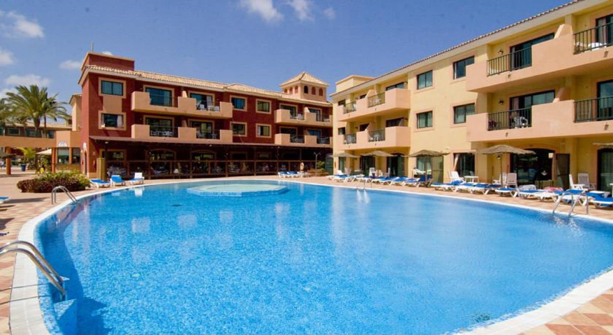 A hotel with a swimming pool surrounded by lounge chairs and a clear blue sky.