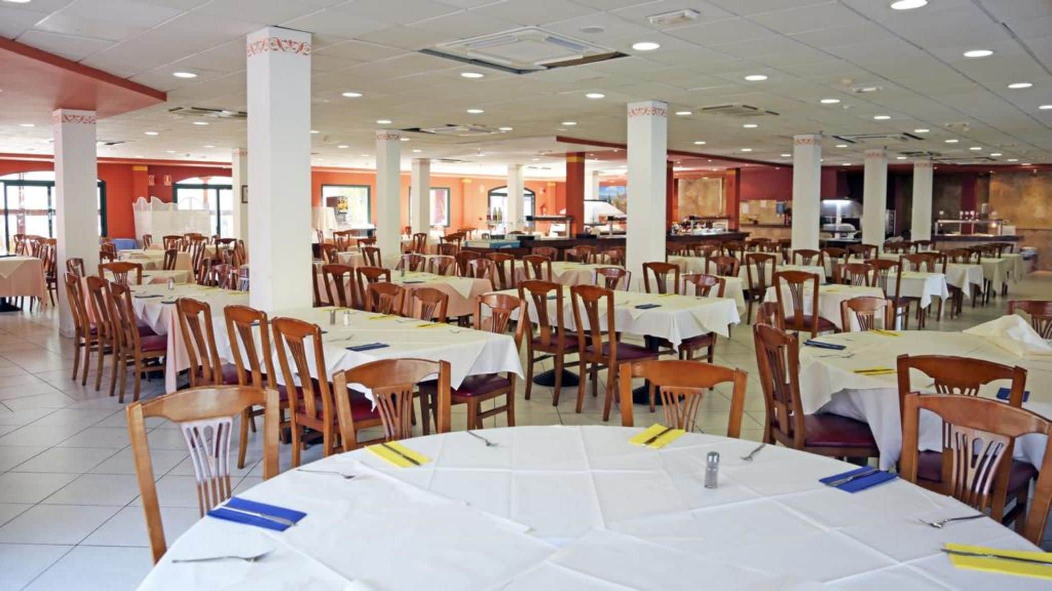 Un comedor amplio con varias mesas y sillas, techos altos y un interior luminoso.