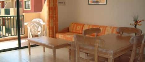 Una habitación con sofá, una mesa de comedor, sillas, un ventanal con vistas a edificios y un cuadro en la pared.