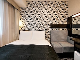 Una habitación de hotel con una cama, una silla, un papel tapiz estampado y una mesita de noche.