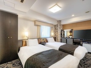 A hotel room with two beds, a desk with a flat-screen TV, a large mirror, and a window with curtains.