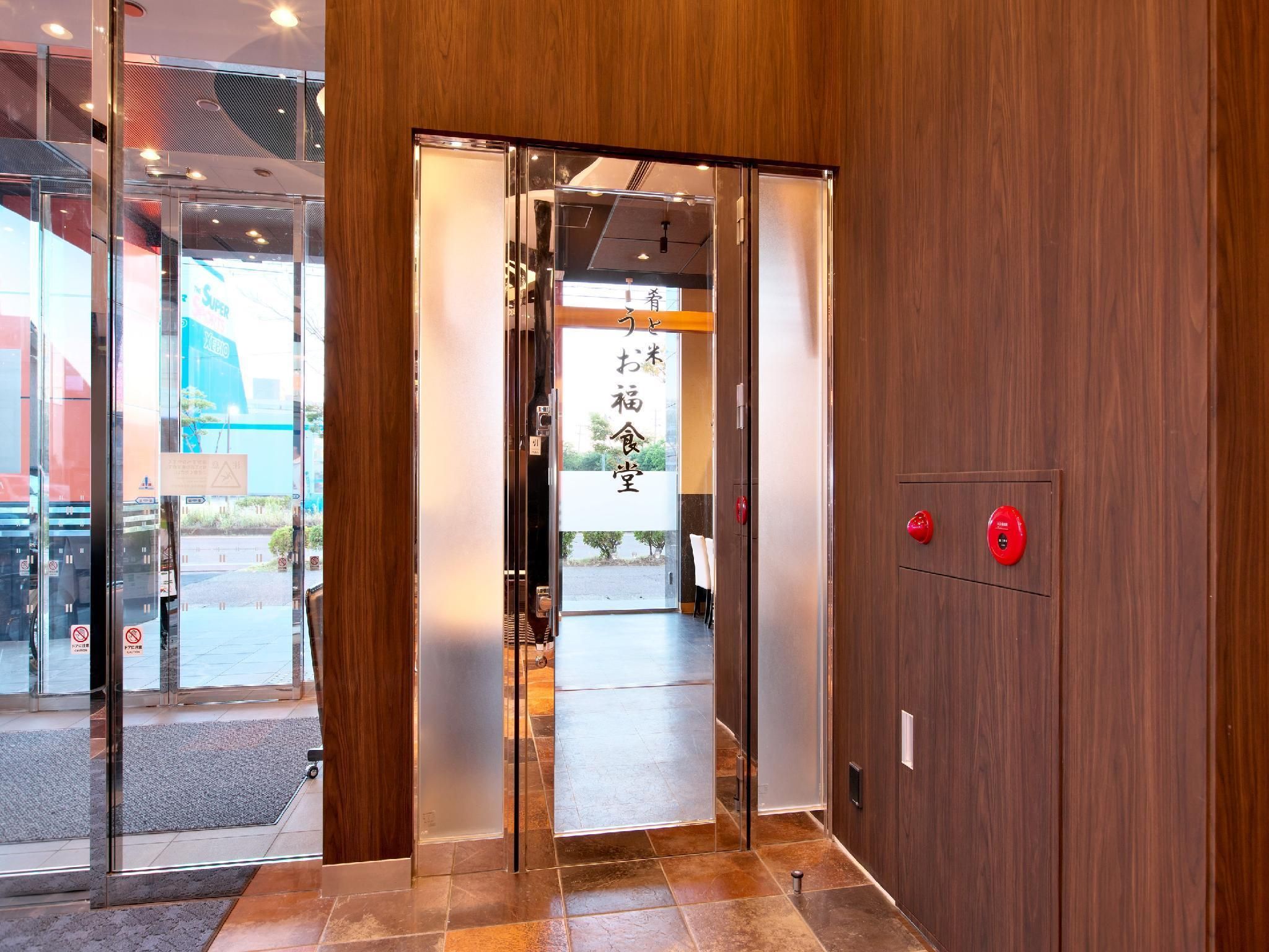 Una entrada de hotel moderna con interior de madera, puertas de cristal y una recepción visible.