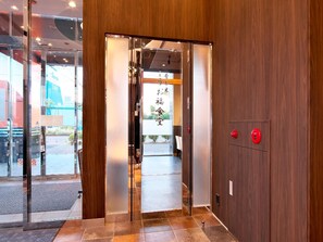 Uma entrada de hotel moderna com interior em madeira, portas de vidro e uma área de recepção visível.