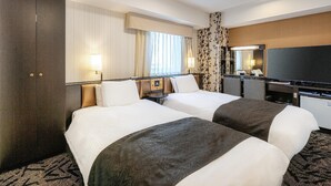 A hotel room with two beds, a desk with a flat-screen TV, a large mirror, and a window with curtains.