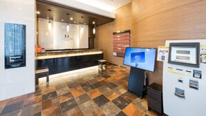 Un espace d’accueil d’hôtel comprenant un comptoir, un écran numérique et un distributeur automatique.