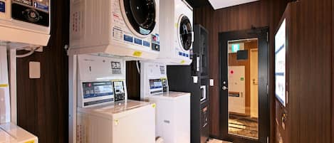 A hotel laundry room with multiple washing machines and dryers, wooden walls, and a patterned floor.
