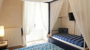 Ein Schlafzimmer mit einem Himmelbett, einem Nachttisch mit Lampe, einem an der Wand befestigten Fernseher und einem Fenster mit Vorhängen.