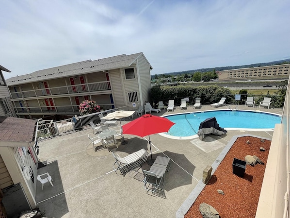 A hotel with a pool area, including lounge chairs and umbrellas. - Sunnyside Inn and Suites (Clackamas)