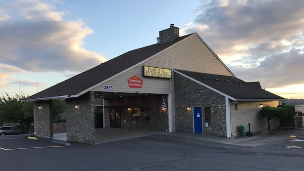 Ein Gebäude mit einer Steinaußenwand, einer blauen Tür und einem Schild, das es als Sunnyside Inn & Suites kennzeichnet.
