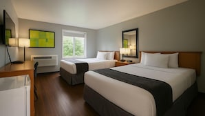 Ein Hotelzimmer mit zwei Betten, einem Schreibtisch, einem Stuhl, einem Fernseher und einem Fenster.
