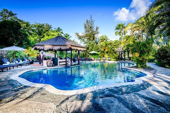 A swimming pool with a thatched-roof gazebo, lounge chairs, and tropical vegetation. - East Winds Inn (Gros Islet)