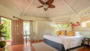 A bedroom with a bed, a ceiling fan, a window with curtains, a door, and a small table with a chair. - East Winds Inn (Gros Islet)