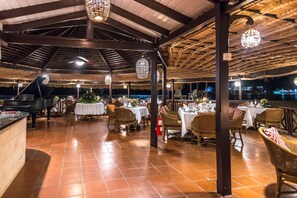 An outdoor dining area with tables and chairs, a piano, and hanging lights. - East Winds Inn (Gros Islet)