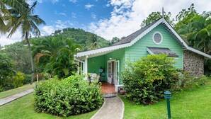 A small green house with a porch, surrounded by lush greenery and a clear sky. - East Winds Inn (Gros Islet)