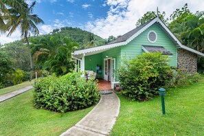 A small green house with a porch, surrounded by lush greenery and a clear sky. - East Winds Inn (Gros Islet)