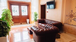 Un hall con un sofá de cuero marrón, una planta en maceta, una puerta grande de madera y un televisor montado.