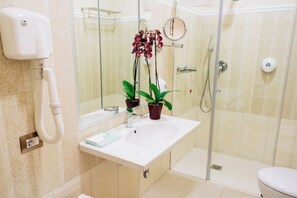 Un baño con un lavamanos blanco, un espejo, un cabezal de ducha manual y dos plantas en macetas.