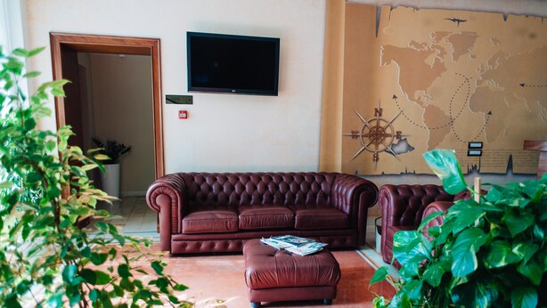 Una sala de estar con un sofá de cuero marrón, un reposapiés a juego, un televisor de pantalla plana, un mapa del mundo en la pared y una puerta que da a otra habitación.