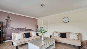 A living room with two sofas, a coffee table, a wall clock, and a mural of a lighthouse. - Host & Stay | Paylors View Cottage (Whitby)