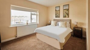 A bedroom with a large bed, a window with a view of a marina, and two paintings on the wall. - Host & Stay | Paylors View Cottage (Whitby)