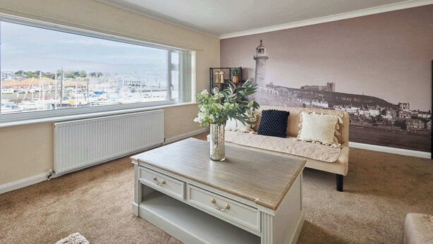 A room with a large window, a sofa, a coffee table, and a mural of a lighthouse. - Host & Stay | Paylors View Cottage (Whitby)