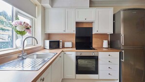 A modern kitchen with white cabinets, a stainless steel refrigerator, a built-in oven, a microwave, and a toaster. - Host & Stay | Paylors View Cottage (Whitby)