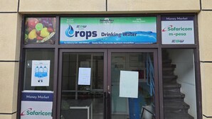 Liiketila, jonka yläpuolella on kyltti, jossa lukee ”Crops Drinking Water”, ja sen alapuolella toinen kyltti, jossa lukee ”Money Market”.