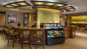 A hotel lobby with a curved reception desk, a coffee station, and a display case with various items. - Sonesta Select Tucson Airport (Tucson)