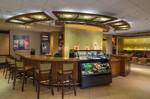 Un hall de hotel con una recepción de forma curva, una estación de café y una vitrina con diversos artículos.