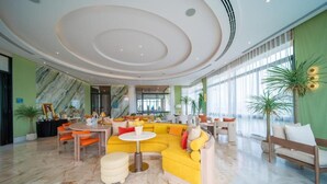 A spacious lobby with a yellow sectional sofa, a round table, and a bench. - Luxury 2BR Pool Apartment in Bang Tao Phuket (Choeng Thale)