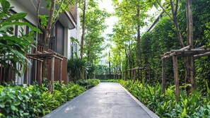 A pathway flanked by lush greenery and wooden structures, leading towards a modern building with large windows. - Luxury 2BR Pool Apartment in Bang Tao Phuket (Tambon Choeng Thale)