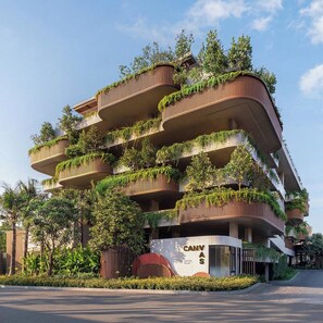Un edifici de diversos pisos amb balcons plens de vegetació, un senyal prominent de 'CANVAS' i una zona d'entrada paisatjada.