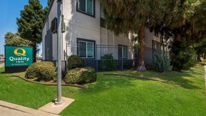 A hotel with a sign reading 'Quality Inn by Choice Hotels,' a well-maintained lawn, and a metal fence.