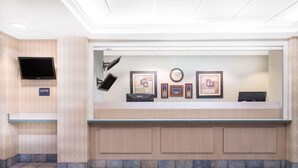 A reception desk with a flat-screen TV, framed artwork, a clock, and a sign indicating a coffee area.
