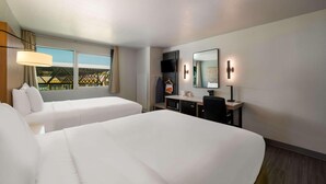 A hotel room with two beds, a desk with a TV, a mirror, and a window with a view.