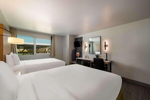 A hotel room with two beds, a desk with a TV, a mirror, and a window with a view.