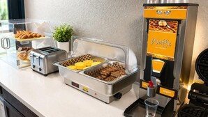 A buffet setup with a waffle maker, toaster, and various food items.