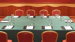 Un salón de conferencias con una larga mesa, sillas rojas, botellas de agua y tarjetas de identificación.