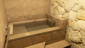 A stone-walled bathroom with a bathtub, a shower area, and a step leading to the shower. - Taoya Nachikatsuura (Nachikatsuura)