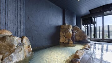 A spa area with a stone wall, a water feature, and a view of the outdoors.