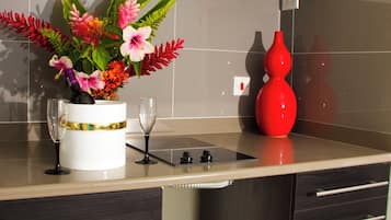 Uma cozinha com armários escuros, bancada branca, um vaso com flores e dois copos de vinho.