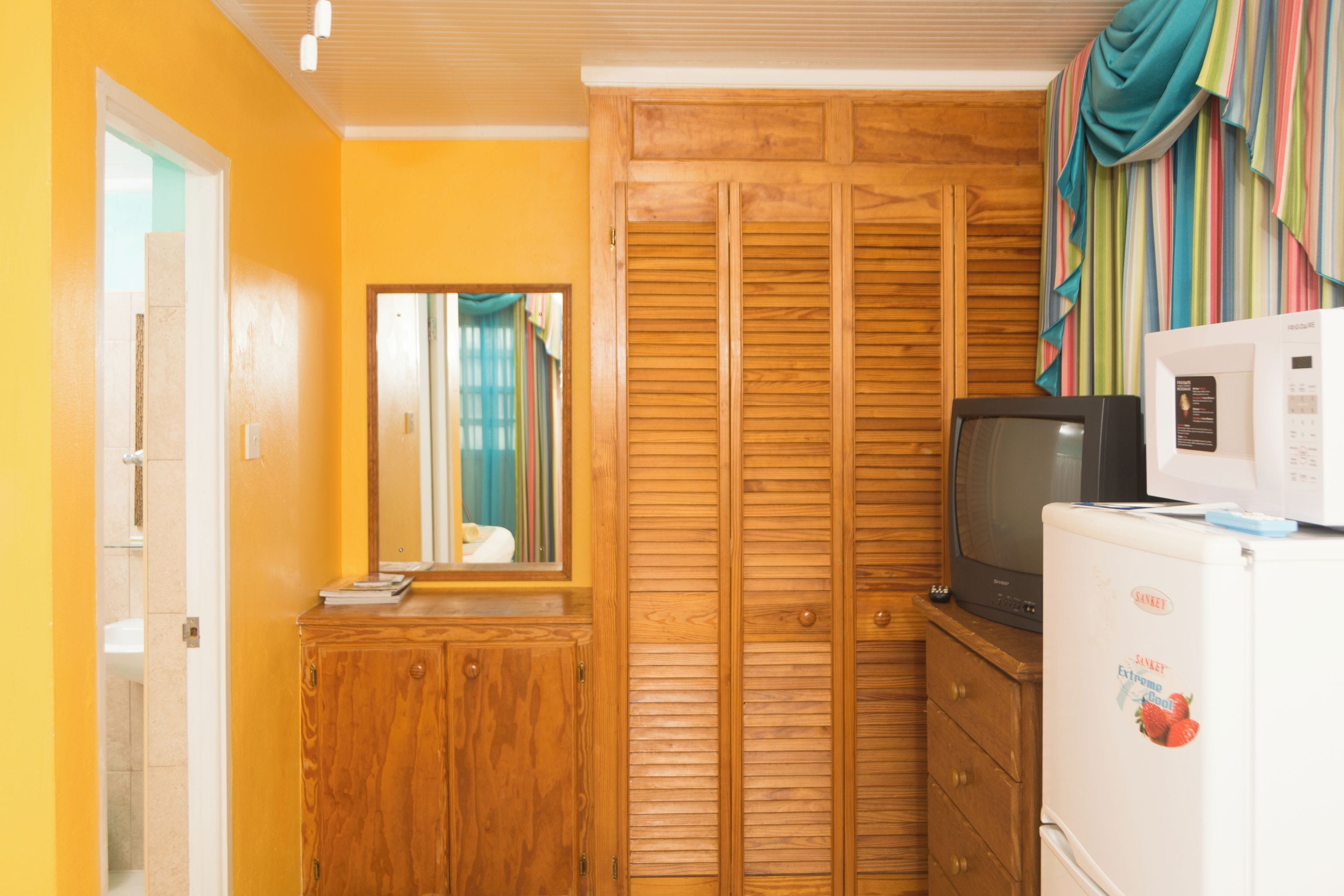 A compact room with a wooden wardrobe, a small cabinet, a television, and a refrigerator.