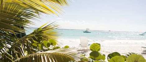 A beach with palm trees, a chair, and a boat in the distance.