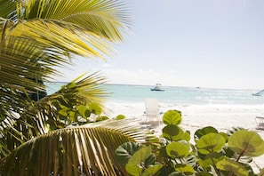 A beach with palm trees, a chair, and a boat in the distance. - Vedanta Resort (Worthing)