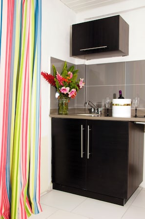 A kitchen with a black cabinet, a vase with flowers, a wine bottle, and two glasses. - Vedanta Resort (Worthing)