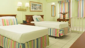 Habitación de hotel con dos camas, una mesita de noche con lámpara, una pequeña mesa con planta y una ventana con cortinas a rayas.