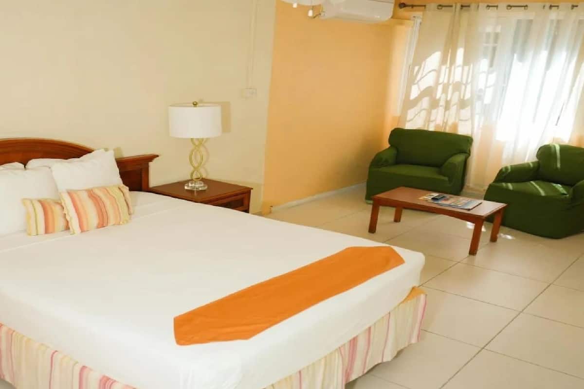 Una habitación de hotel con una cama grande, un sillón verde, una mesita y una lámpara.
