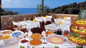 Ein Essbereich im Freien mit Tischen, die für ein Frühstück gedeckt sind, mit Blick auf das Meer.